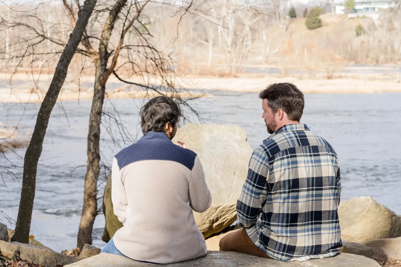 Two men sitting on rocks beside the James River, talking