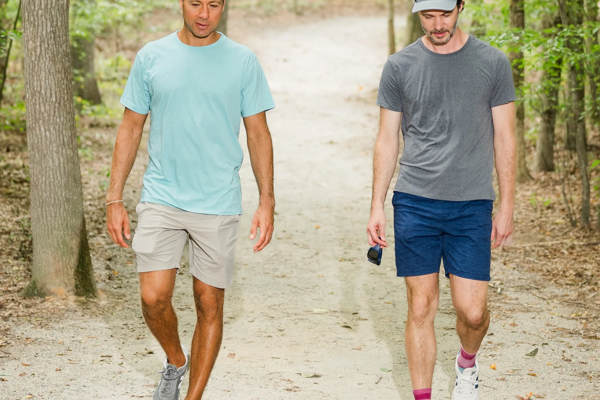 Two men walking a sunlit wooded trail toward the camera at Pony Pasture